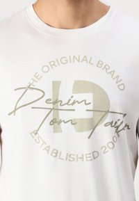 Hvit bomulls t-skjorte med grafisk design i lysegrønn tekst, med "Denim Tom Tailor" og en etablert dato fra 2007 i sirkulært format.