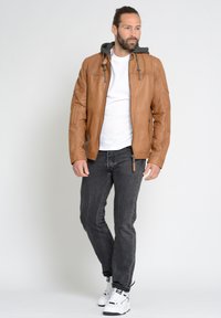 Braune Lederjacke mit grauem Kapuzen, Reißverschluss vorne und seitlichen Taschen. Kombiniert mit grauen Jeans und weißen Sneakers. Lässiges Design.