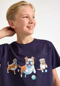 Mørkeblå bomulds-T-shirt med tre illustrerede hunde i rumtema, omgivet af stjerner og planeter. Glat tekstur, rund halsudskæring.