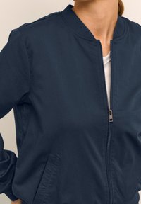 Chaqueta bomber azul marino con cremallera frontal, cuello acanalado y bolsillos laterales. Confeccionada con tela suave y diseño ligero.