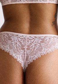 String en dentelle de couleur rose doux avec un motif floral, des bords festonnés et une taille lisse. Tissu texturé avec des détails intricats.