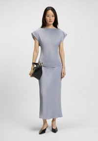 Abito lungo, setoso, di un leggero colore lavanda con maniche corte a sbuffo. Abbinato a una borsa nera con un dettaglio in oro circolare. Mule nere con tacco.