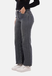 Jeans a vita alta, dritti, in denim blu scuro. Presentano tasche frontali, chiusura con bottone metallico e cuciture decorative. Abbinati a sneakers bianche.