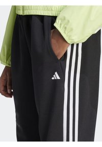 Schwarze Sporthose mit drei weißen Streifen an den Seiten, ausgestattet mit einer Seitentasche und einem weißen Adidas-Logo auf dem Oberschenkel.