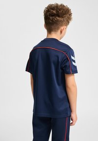 Marinblå idrottströja med korta ärmar, med röd kantstickning och en logotyp på vänster ärm. Slät, andningsbar tyg.