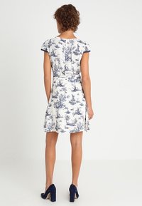 Kortärmad klänning i vitt tyg med blå blommönster, med en figurnära midja och utsvängd kjol med en sidofåra.