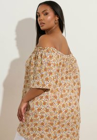 Blusa scollata in bianco con un motivo floreale arancione, giallo e verde. Vestibilità ampia con maniche corte e scollo elastico.