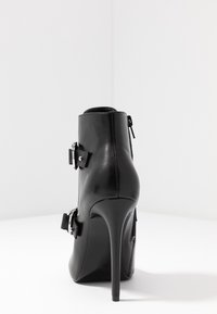 Czarne skórzane botki za kostkę na wysokim obcasie w kształcie szpilki, z metalowymi srebrnymi klamrami i zapięciem na zamek. Gładka tekstura i elegancki design.