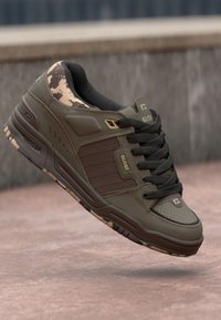 Olive green skate shoes with a camouflage pattern at the toe, lace-up design, and textured rubber sole with brown accents.