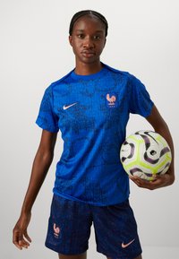 Blue sports jersey and shorts featuring a textured pattern, with a rooster emblem and a Nike logo. Holding a multi-colored soccer ball.