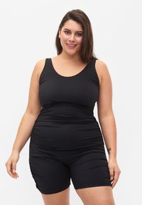 Maillot de bain une pièce noir avec un décolleté en forme de scoop et des détails ruchés, présentant une coupe ajustée et se prolongeant jusqu'à mi-cuisse.
