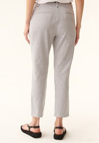 Pantalons rayés à coupe ajustée, en tissu léger, avec une taille mi-haute et deux poches arrière. Portés avec des sandales plates.