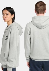 Lyst grå hættejakke med kængurulomme og broderet logo; lavet af blødt stof med ribbet manchetter og kant.