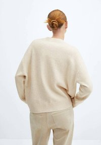 Pull en maille beige avec poignets et ourlet côtelés, coupe ample et texture douce, associé à un pantalon en daim beige clair. Vue de dos.