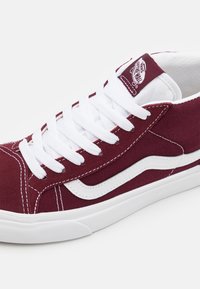 Baskets basses Vans bordeaux avec lacets blancs, bande latérale blanche et semelle en caoutchouc, affichant le logo sur la languette.