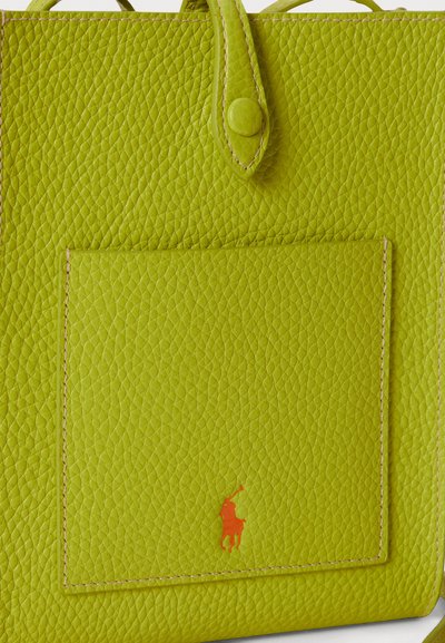 Torbo iz limetino zelene usnja z ročaji na vrhu, sprednjim žepom in oranžnim logotipom kot detajlom, z teksturirano površino.