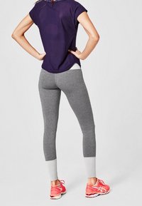 Szare legginsy sportowe o dopasowanym kroju z kontrastującymi jasnoszarymi mankietami, zestawione z luźną fioletową bluzą i różowymi butami do biegania.