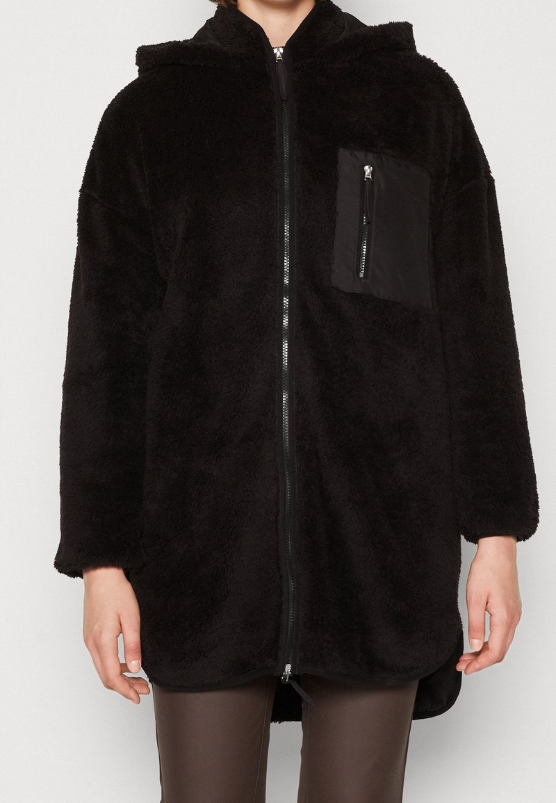 Chaqueta de forro polar con capucha negra, con cierre frontal de cremallera, textura suave, bolsillo tipo canguro y un bolsillo de contraste en la parte superior izquierda.