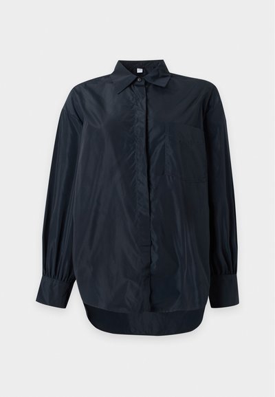 Chemise noire à manches longues, boutonnée, avec col et poche poitrine, présentée sur un fond clair uni.
