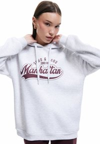 Jasnoszara bluza z kapturem z burgundowym nadrukiem "Manhattan", sznurkami i ściągaczami na rękawach. Miękka tkanina o swobodnym fasonie.