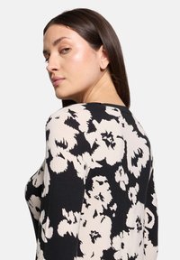 Czarna i kremowa bluzka w kwiatowy wzór z okrągłym dekoltem i długimi rękawami, wykonana z gładkiego materiału, o dopasowanym kroju.