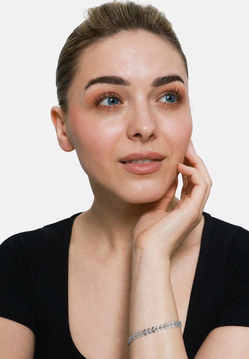 Braccialetto d'argento con design a foglia, indossato al polso. Il soggetto ha la pelle chiara, occhi azzurri e indossa un top nero.