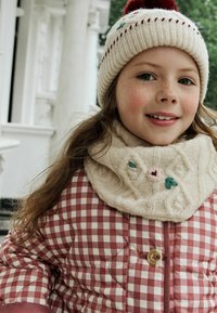 Rød og hvid ternet puffjakke med en stor knap, en cremet strikket tørklæde med blomsterbroderi, og en beige strikket hat med en pompon.