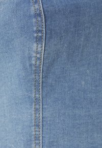 Lyseblå denimstoff med synlig tekstur, med kontrastfarget brun søm langs en søm, som fremhever plaggets konstruksjon.