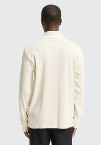 Lange mouwen shirt in crème, met een geribbelde textuur, hoge kraag en een licht gebogen zoom. Eenvoudig en veelzijdig ontwerp.