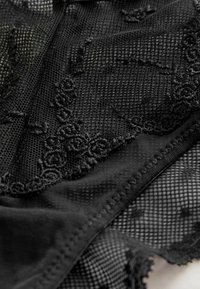 Black lace lingerie featuring a mesh design with floral embroidery, soft fabric texture, and contrasting sheer and solid sections.