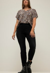 Top holgado de estampado de leopardo, jeans negros ajustados, botines negros con detalle de cadena. Escote en V, mangas cortas, textura suave.