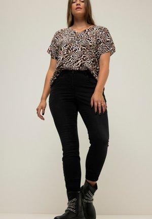 Top holgado de estampado de leopardo, jeans negros ajustados, botines negros con detalle de cadena. Escote en V, mangas cortas, textura suave.