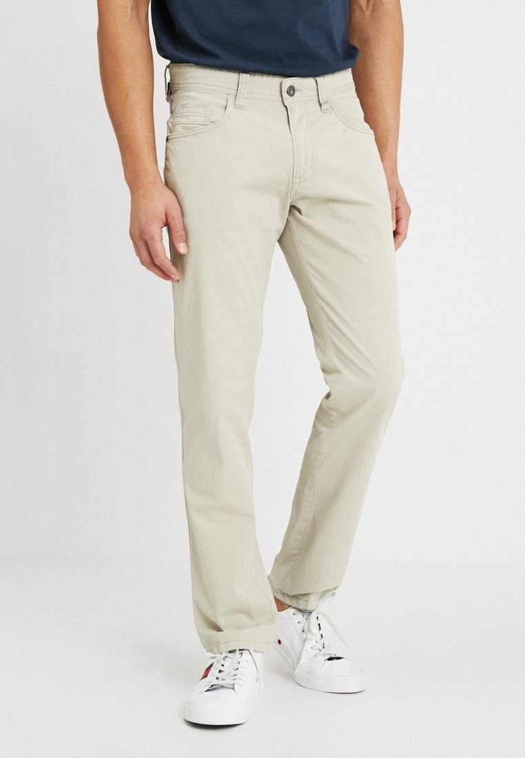 Pantalones de cotón beige con diseño de pierna recta, que cuentan con bolsillos laterales, un cierre de botón y detalles de costura sutiles, combinados con zapatillas blancas.