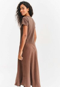Brązowa sukienka do kolan z krótkimi rękawami, wykonana z miękkiej tkaniny. Charakteryzuje się prostym fasonem i zwiewnym kształtem, odpowiednia na co dzień.