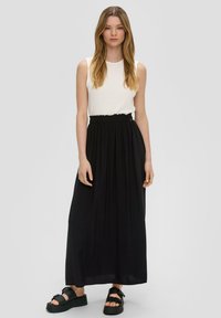Witte, textuurloze, mouwloze top gecombineerd met een vloeiende zwarte maxi rok met een elastische taille, gedragen met zwarte platform sandalen.