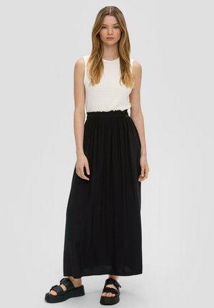 Haut sans manches blanc texturé associé à une jupe maxi noire fluide avec une taille élastique, portée avec des sandales à plateforme noires.
