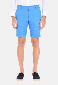 Pantaloni corti blu in lino con risvolti, caratterizzati da una parte anteriore piatta, passanti per la cintura e una consistenza liscia. Indossati con mocassini scuri.