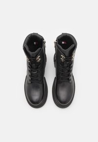 Bottines en cuir noir à finition lisse, avec des accents de quincaillerie dorée, des lacets et des fermetures éclair latérales pour un port facile.