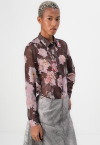 Gjennomsiktig brun skjorte med rosa blomstermønster, kontrasterende knapper og klassisk krage; kombinert med en teksturert grå skjørt.