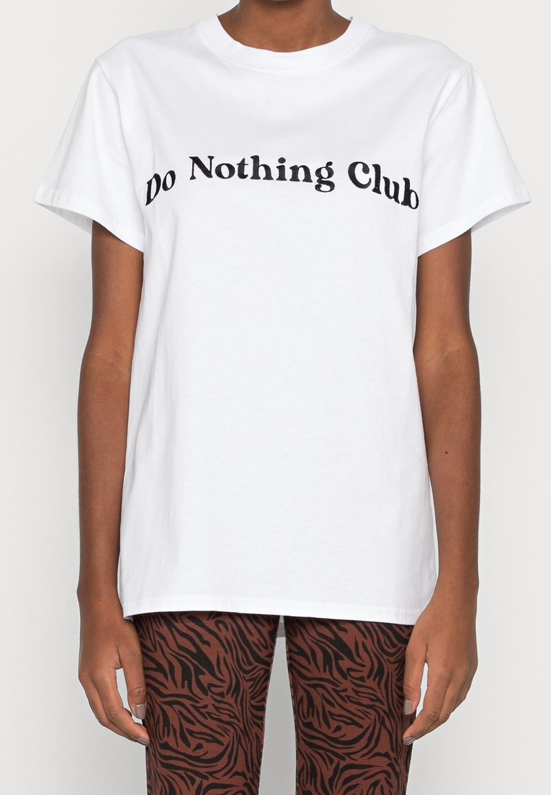 Vit bomullströja med en böjd svart textdesign "Do Nothing Club" över bröstet, med en avslappnad passform och korta ärmar.