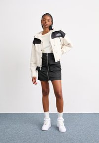 Cropped cream and black jacket with a hood, paired with a black zip skirt. White high-top sneakers and white textured socks.
