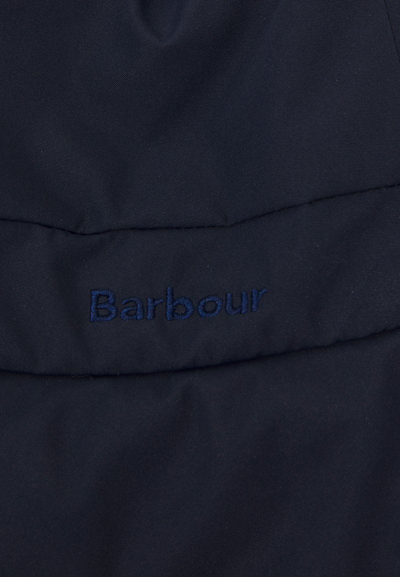 Primer plano de una tela de color azul oscuro con el logotipo de Barbour en color azul marino bordado en una sección acolchada.