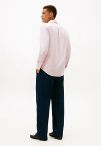 Camicia a maniche lunghe a righe in rosa chiaro con polsini abbottonati, abbinata a pantaloni a gamba larga in blu scuro. Tasca anteriore visibile, orlo della camicia curvo.