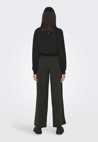 Haut noir à manches longues, associé à un pantalon large vert foncé. Tissu lisse avec une taille élastique. Design subtil et peu de détails.