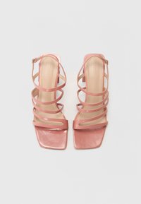 Pink heeled sandals featuring multiple thin straps and a square toe. Made from glossy material with a textured insole and ankle strap.