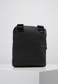 Borsa a tracolla nera con corpo in tessuto e fondo in pelle. Presenta spallacci regolabili e un design elegante e minimalista.