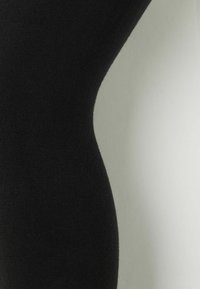 Leggings neri realizzati in un tessuto liscio e elasticizzato. Il design presenta una forma aderente con una vita senza cuciture e una leggera texture in tutto il capo.