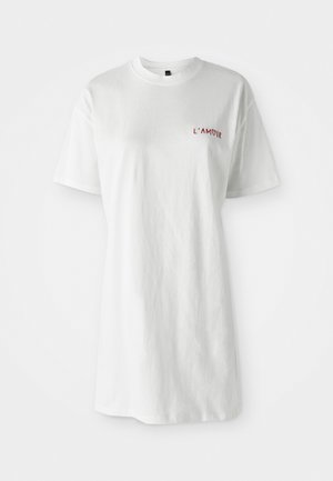 Vit t-shirt med kort ärm med "L'AMOUR" broderat i rött på vänster bröst, visad mot en enfärgad vit bakgrund.