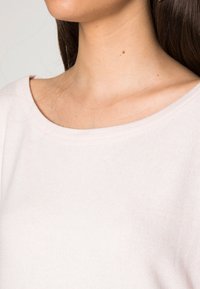 Top de tecido canelado, rosa claro, com um amplo decote arredondado. A imagem em close destaca a textura suave e os detalhes finos do material.