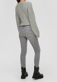 Pull gris côtelé à manches larges associé à un jean gris slim. Le mannequin porte des bottes noires à lacets avec des semelles épaisses.